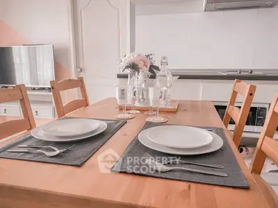 Charming dining area with wooden table set for two, modern kitchen in background.