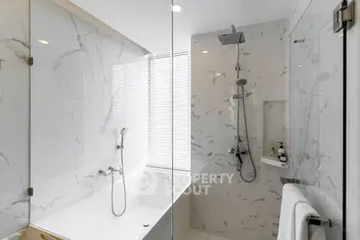 Luxurious modern bathroom with marble walls and sleek fixtures, featuring a spacious bathtub and rain shower.