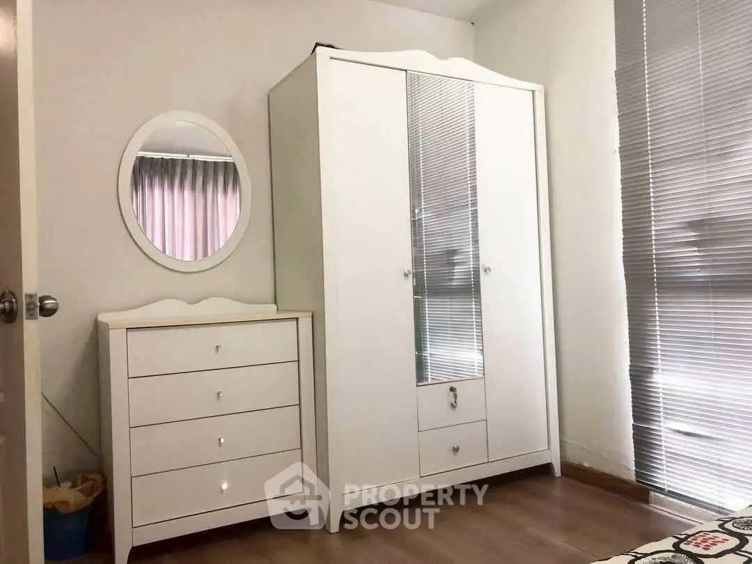 Cozy bedroom with white wardrobe and dresser, featuring modern blinds and wooden flooring.