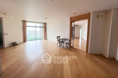 Spacious open-plan living area with wooden flooring and large windows offering city views.