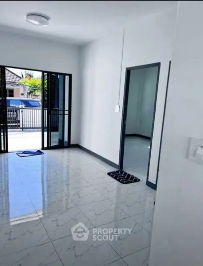 Spacious living room with glossy tiled floors and sliding glass doors leading to a bright outdoor area.