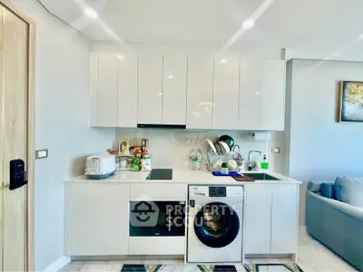 Modern kitchen with sleek white cabinets, integrated appliances, and cozy living area.