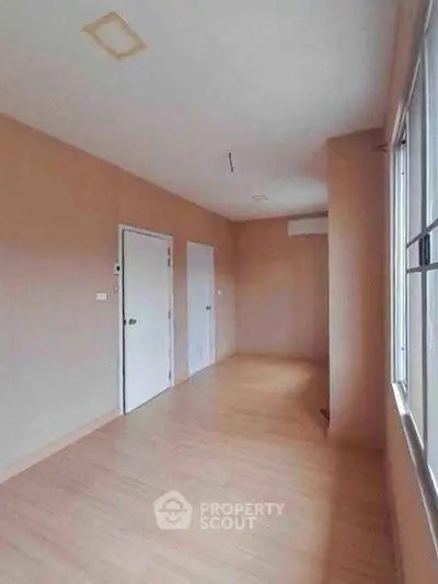 Spacious empty room with wooden flooring and large windows, ideal for customization.
