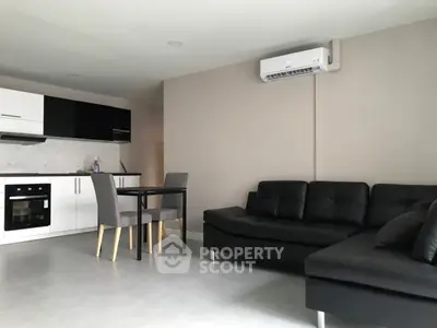 Modern open-plan living room with sleek black sofa and stylish kitchen area.