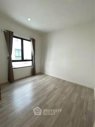 Spacious empty room with large window and elegant wood flooring, perfect for customization.