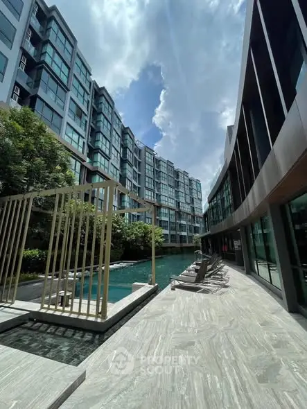 Modern apartment complex with pool and stylish architecture under a bright sky.