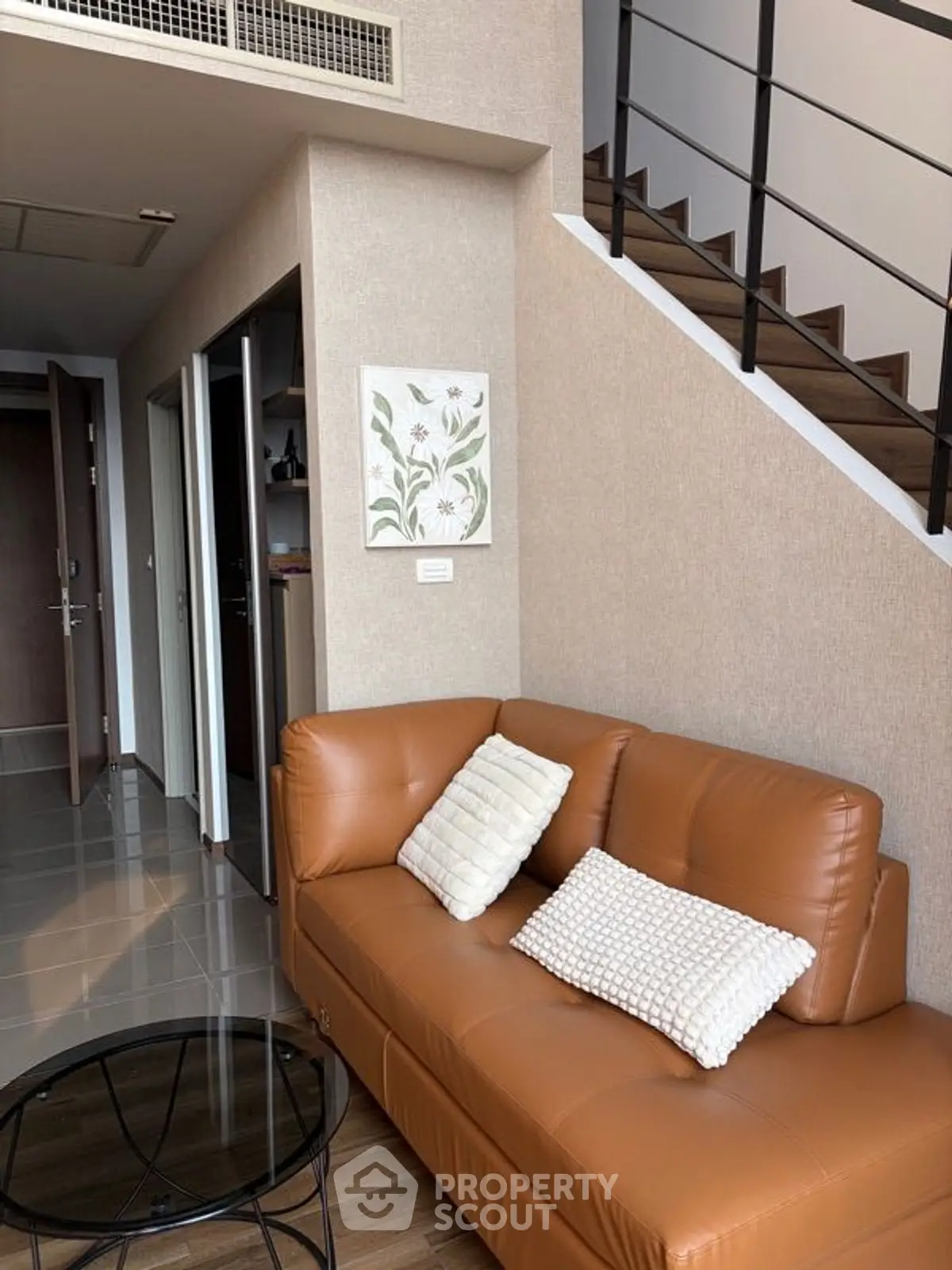 Modern duplex living room with stylish brown leather sofa and elegant staircase.