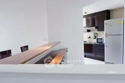 Modern kitchen with dark wood cabinets and stainless steel fridge in open layout design.