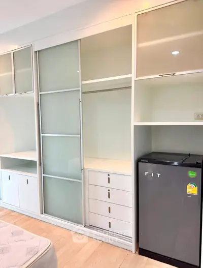Modern bedroom with built-in wardrobe and compact fridge, showcasing efficient use of space.