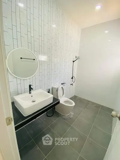 Modern bathroom with sleek design featuring a round mirror, square sink, and tiled walls.