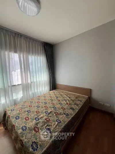 Cozy bedroom with large window and elegant curtains, featuring a stylish bedspread.