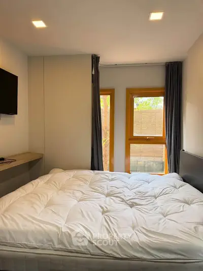 Cozy bedroom with large bed, wall-mounted TV, and natural light from two windows.