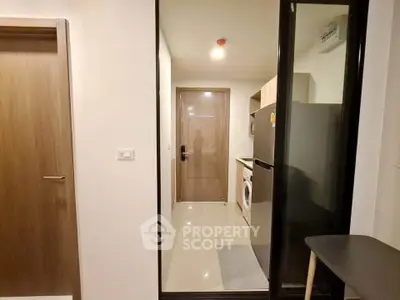 Modern apartment entryway with sleek kitchen appliances and stylish wooden door.