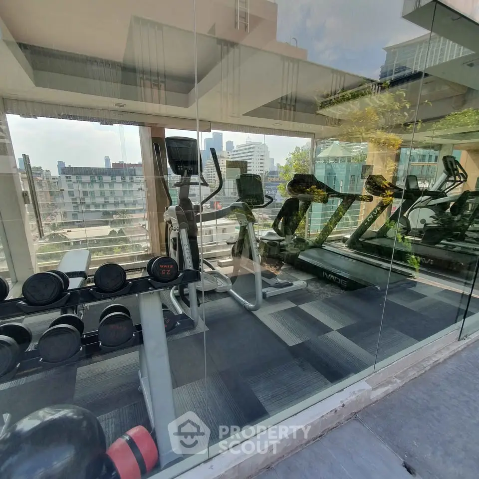 Modern gym with city view featuring treadmills and weights in a glass-walled fitness center.