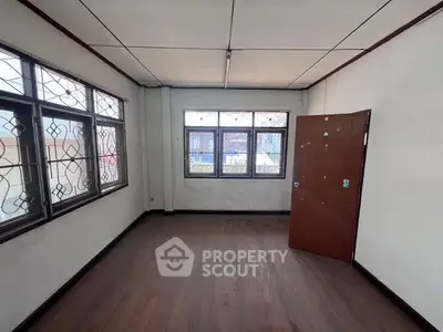 Spacious empty room with wooden floors and large windows in a residential property.