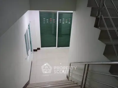 Modern staircase with sleek metal railing and tiled flooring in a contemporary building.