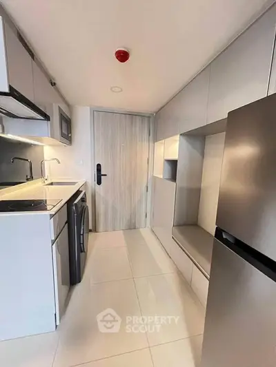 Modern kitchen with sleek cabinetry, washing machine, and stainless steel fridge in compact layout.