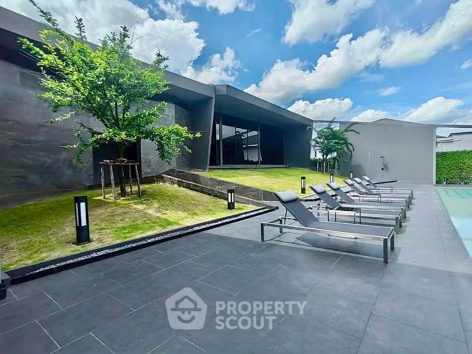 Luxurious modern rooftop with sun loungers and lush greenery under blue skies.