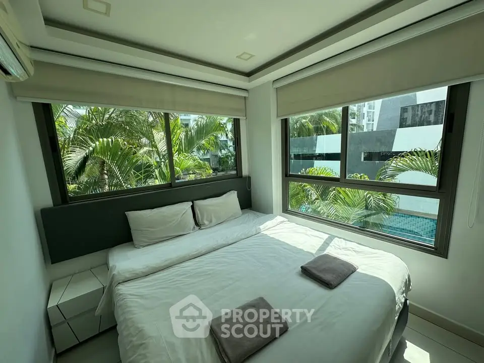 Modern bedroom with large windows and pool view, featuring a cozy bed and lush greenery outside.
