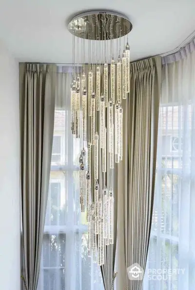 Elegant modern chandelier in a luxurious living room with floor-to-ceiling windows and stylish curtains.