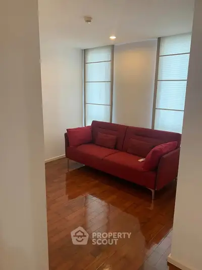 Cozy living room with red sofa and wooden flooring, perfect for relaxation.