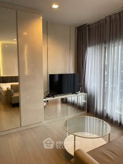 Modern living room with sleek design, featuring a large TV, elegant curtains, and a glimpse of a cozy bedroom.