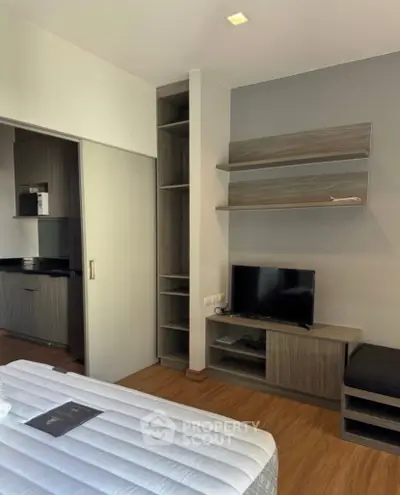 Modern bedroom with sleek built-in shelves and compact TV unit, adjacent to a stylish kitchen area.