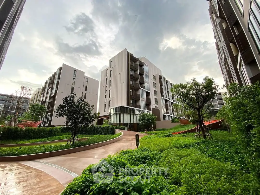 Modern residential building with lush green landscaping and cloudy sky backdrop.