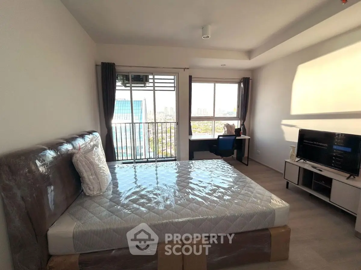 Modern bedroom with large windows and city view, featuring a bed and desk setup.