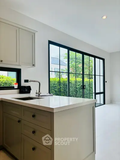 Modern kitchen with sleek cabinetry and large windows overlooking lush greenery.
