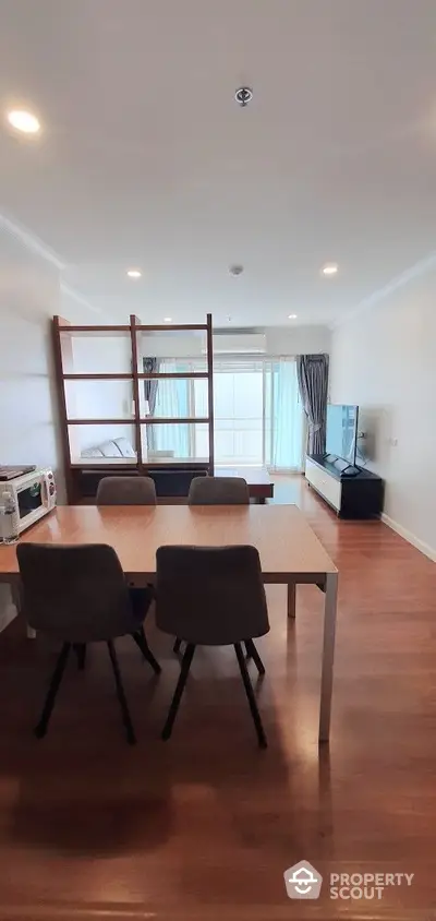 Spacious and well-lit living room with polished wooden floors, modern furniture, and a cozy dining area leading to a sunlit balcony.