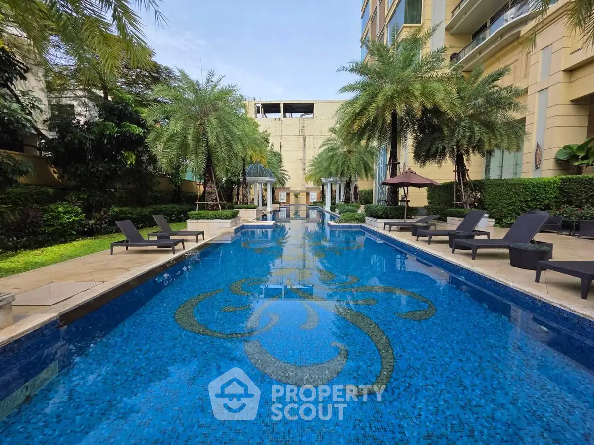 Luxurious outdoor pool area with palm trees and sun loungers in a modern residential complex.