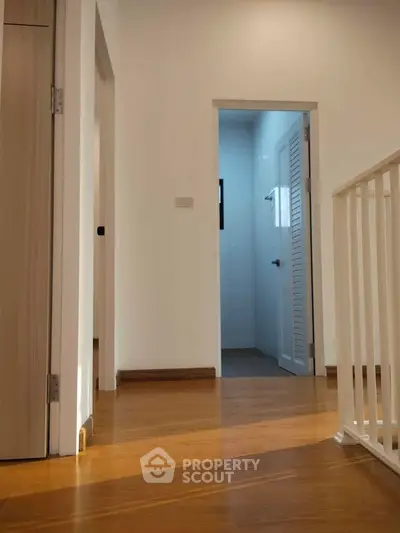 Bright hallway with wooden flooring leading to a bathroom, showcasing modern interior design.
