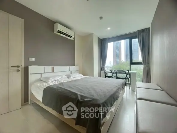 Modern bedroom with large window and city view, featuring sleek furniture and neutral tones.