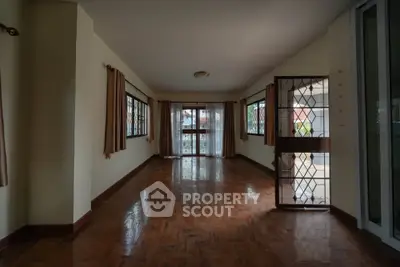 Spacious living room with large windows and wooden flooring, perfect for natural light and comfort.