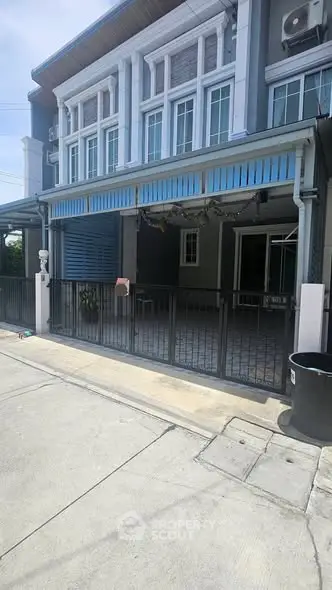 Charming townhouse exterior with gated entrance and blue awning, perfect for modern living.