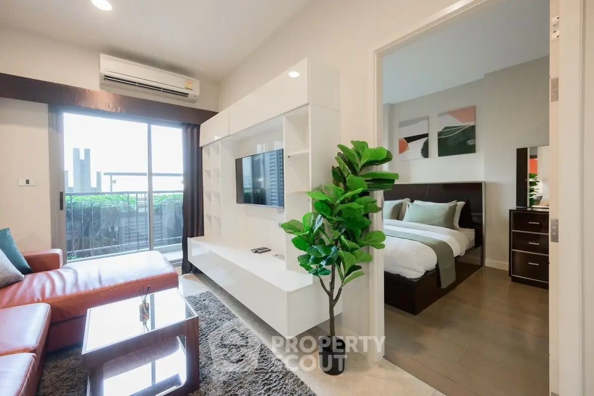 Modern living room with sleek furniture and a view into a cozy bedroom, featuring a large window and stylish decor.