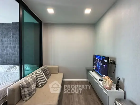 Modern living room with cozy sofa and TV, adjacent to a bedroom with glass partition.