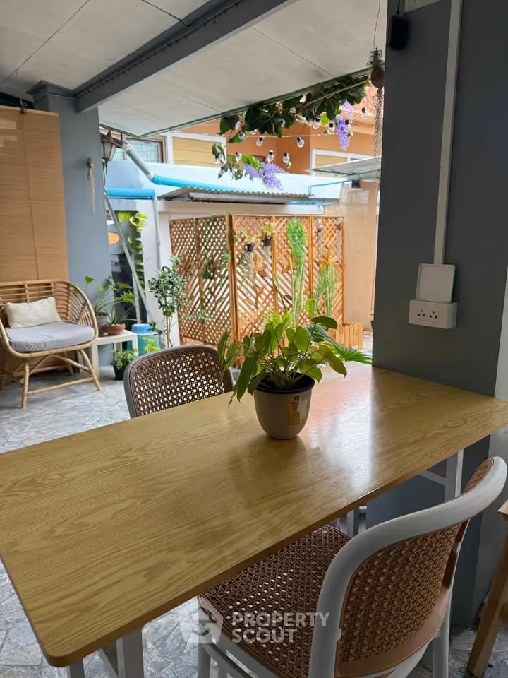 Charming outdoor patio with wooden table and chairs, surrounded by lush greenery and cozy seating area.