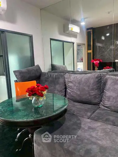 Modern living room with plush gray sofa and elegant glass table, accented by vibrant red flowers.