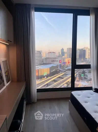 Modern bedroom with city view, featuring a cozy workspace and large window for natural light.