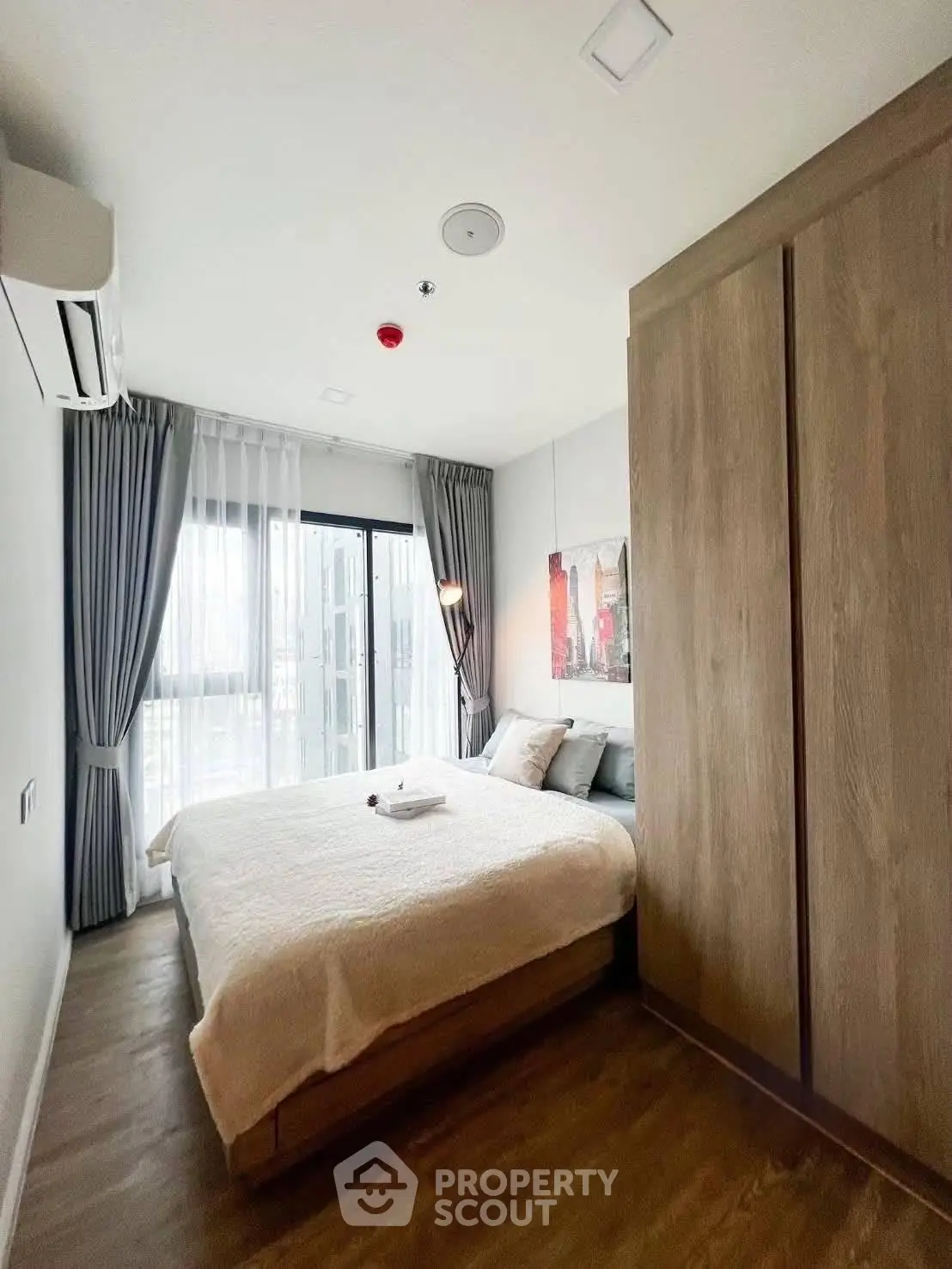 Modern bedroom with large window, wooden flooring, and stylish decor in a cozy apartment.