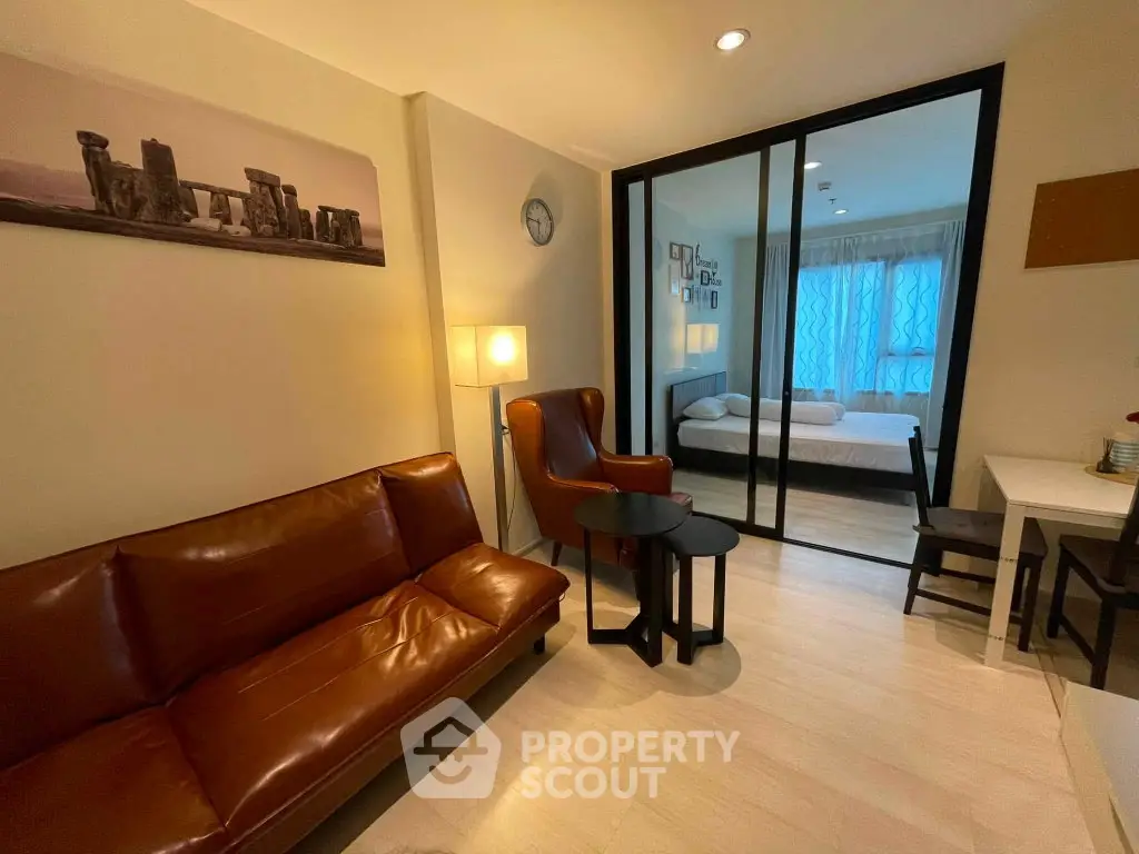 Modern apartment interior with cozy living room and bedroom separated by glass doors, featuring stylish furniture.