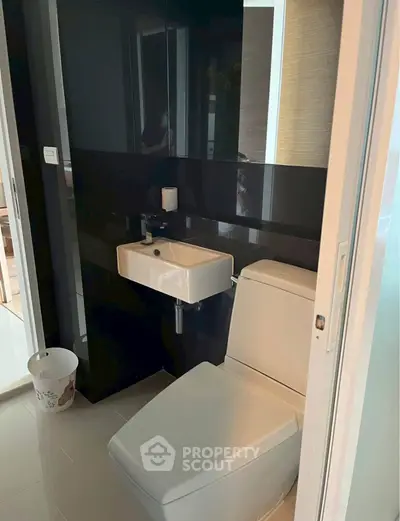 Modern compact bathroom with sleek black and white design, featuring a toilet and small sink.