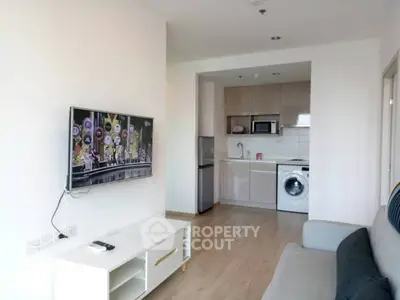 Modern living room with open kitchen, featuring a wall-mounted TV and sleek appliances.