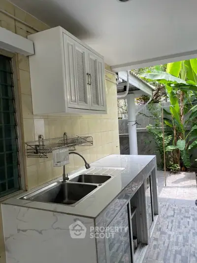 Modern outdoor kitchen with marble countertop and stainless steel sink in a lush garden setting.