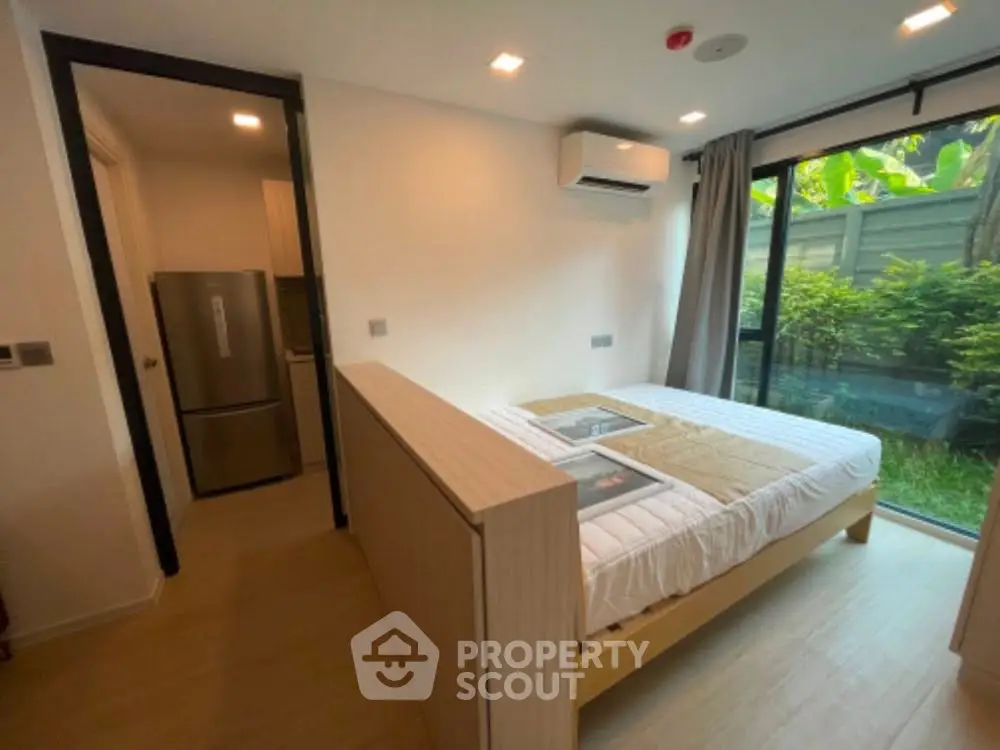 Modern bedroom with garden view and air conditioning, featuring a cozy bed and sleek refrigerator.