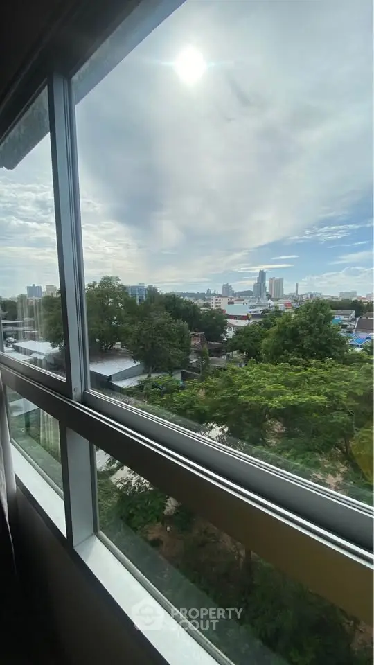 Stunning cityscape view from a modern apartment window, showcasing lush greenery and urban skyline.