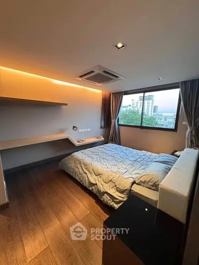 Modern bedroom with large window and wooden flooring, featuring a cozy bed and built-in shelves.