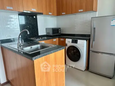 Modern kitchen with wooden cabinets, granite countertops, and appliances including fridge and washing machine.
